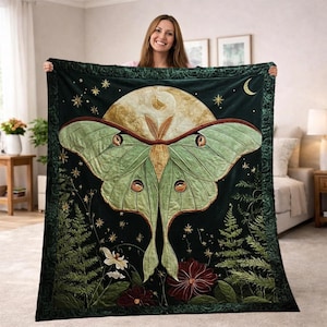 May include: A dark green throw blanket featuring a large moth design with a full moon backdrop. The moth has green wings with brown and yellow details. The blanket also includes floral and celestial elements.