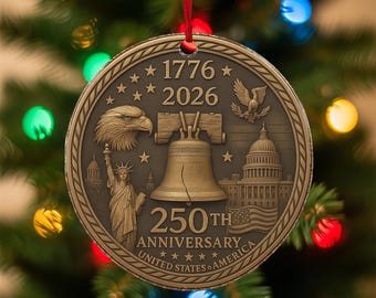 May include: A bronze-colored round Christmas ornament with a red ribbon. The ornament features the text "1776 2026" and "250th Anniversary United States of America". The design includes an eagle, the Liberty Bell, the Statue of Liberty, and the Capitol Building.