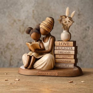 May include: A wooden figurine depicting a mother and child reading a book. The sculpture is light brown with a stack of books labeled "Love," "Laughter," "Dreams," "Adventures," "Hugs," "Kindness," and "Family." A small vase with dried flowers sits atop the books.