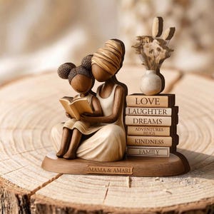 May include: A wooden figurine depicts a mother and child reading a book. The figurine is light brown with a stack of books labeled "Love, Laughter, Dreams, Adventures, Hugs, Kindness, Family." The base reads "Mama & Amari."