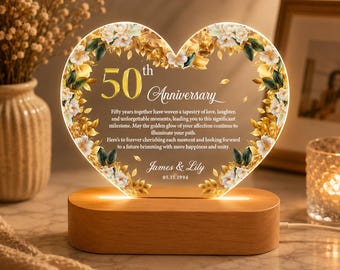 May include: A heart-shaped, illuminated anniversary gift with floral accents. The clear acrylic piece displays "50th Anniversary" and personalized text, set on a wooden base. The design includes gold and white flowers, with the names "James & Lily" and a date.