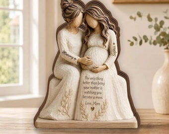 May include: A cream-colored figurine of two figures, one seated and one standing, with carved textures. The standing figure has a pregnant belly. Text on the figures reads: Mommy, Sophia, and The only thing better than being your mother is watching you become a mom. Love, Mom.