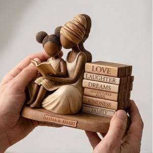 May include: A wooden figurine depicting a mother and child reading a book. The figurine is light brown with a stack of books on the right side. The books have words like "Love" and "Family" on them. The base of the figurine reads "Mama & Amari."