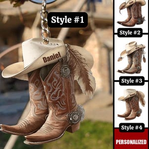 Könnte beinhalten: Ein brauner Cowboy-Stiefel- und Hut-Schlüsselanhänger mit dem Namen "Daniel" auf dem Hut. Der Schlüsselanhänger hat eine silberne Kette und eine Feder. Das Bild zeigt auch drei weitere Stile von personalisierten Cowboy-Stiefel- und Hut-Schlüsselanhängern.