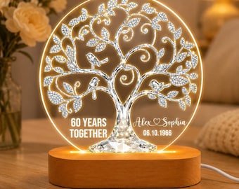 May include: A lighted, round acrylic tree sculpture with a wooden base. The tree design features sparkling crystals and two birds. Text on the sculpture reads "60 YEARS TOGETHER" and "Alex & Sophia 06.10.1966".