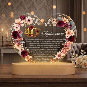 May include: A heart-shaped anniversary gift with floral accents and the text "40th Anniversary." The clear acrylic piece sits on a wooden base, illuminated from below. The text includes a personalized message and date.