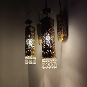 Antique brass wall lamp with pierced metal shade casting decorative shadows