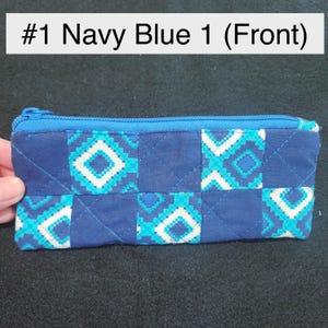 May include: Navy blue zippered pencil case with a geometric pattern in white and turquoise. The case is quilted and has a navy blue zipper. The text "#1 Navy Blue 1 (Front)" is at the top.