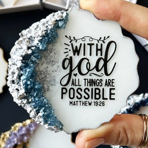 May include: A white ceramic coaster with a blue and silver epoxy resin design. The coaster features the text "With God all things are possible" and the Bible verse "Matthew 19:26".