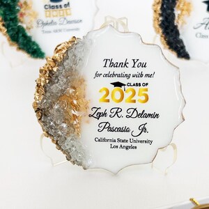 Op de afbeelding: Afstudeerbedankjes met gouden accenten. De afbeelding toont drie decoratieve stukken met de tekst "Bedankt" en "Klasse van 2025". Ook inbegrepen zijn waszegels, een lakstempel en een geschenkdoos met een koekje met een afstudeerthema.