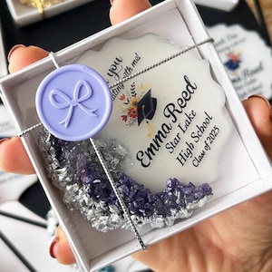 May include: A white ceramic coaster with a purple wax seal and a graduation message for Emma Reed. The message reads "Emma Reed, Star Lake High School, Class of 2023".