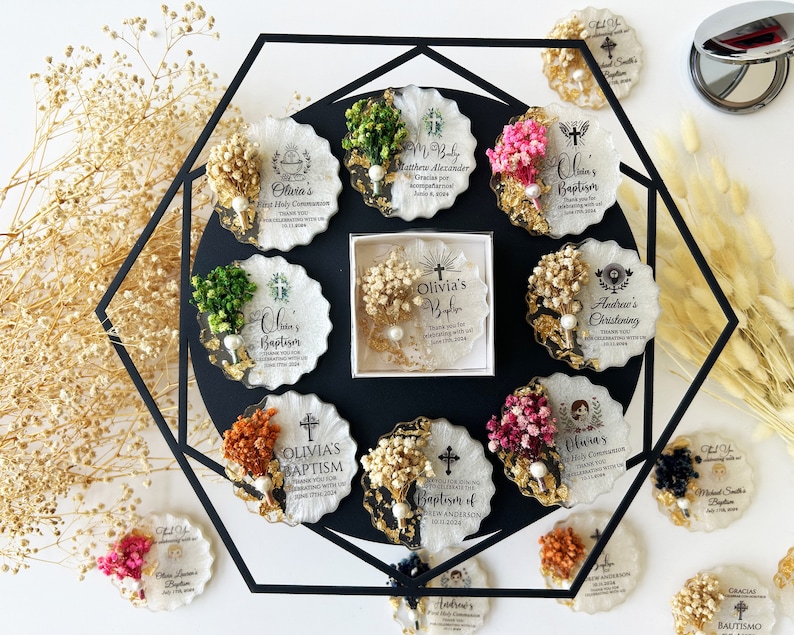 May include: A collection of personalized baptism and first communion favors. Each favor is a unique, scalloped-edged coaster with dried flowers, gold leaf accents, and a pearl. The favors feature names and dates.