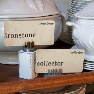 May include: Two white wooden signs with black text on a brown wooden shelf. The signs are labeled "ironstone" and "collector".