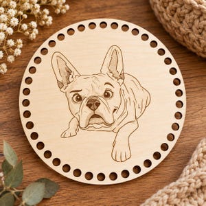 Könnte beinhalten: Eine kreisförmige Basis aus hellem Holz mit einer lasergravierten Illustration einer Französischen Bulldogge. Die Holzscheibe weist eine Reihe von gleichmäßig verteilten Löchern entlang des gesamten Außenrandes auf, die zum Basteln dienen.