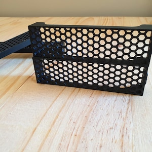 Puede incluir: Dos paneles de plástico negro con un patrón de panal. Los paneles están apilados uno encima del otro.