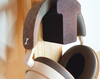 Op de afbeelding: Witte en bruine over-ear koptelefoon hangend aan een houten koptelefoonstandaard met een bruin schuimkussen.
