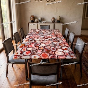 May include: A rectangular dining table featuring a tabletop composed of numerous polished, multi-colored red and white agate stone slices. The table is supported by a dark metal frame and is surrounded by six grey upholstered chairs with wooden legs.