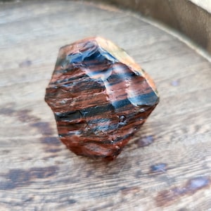 May include: A polished, multi-faceted stone with a striking pattern of deep red, black, and hints of blue. The stone's surface reflects light, showcasing its natural textures and colors. The stone is a unique decorative item.