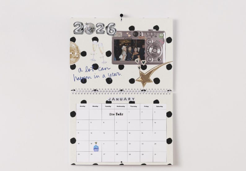 May include: A spiral-bound calendar for the year 2026, featuring a January page with a polka dot design. The calendar includes a photo, a gold star, and the handwritten phrase "a lot can happen in a year."
