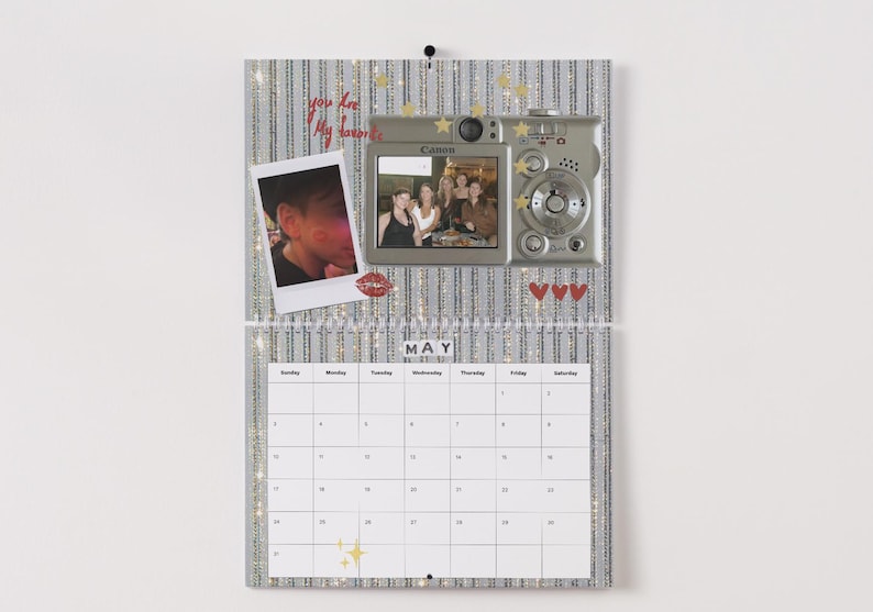 May include: A decorative calendar with a silver and white striped background. It features a photo of a person, a digital camera, and a photo of a group of people. The calendar displays the month of May and has a grid of dates.