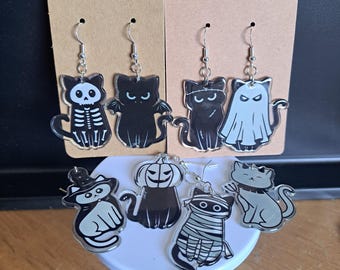Puede incluir: Un conjunto de pendientes de gato con temática de Halloween. Los diseños incluyen un gato esqueleto, un gato murciélago, un gato fantasma, un gato bruja, un gato calabaza, un gato momia y un gato gris. Cada pendiente tiene un gancho plateado.