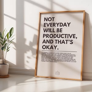 Può includere: Un poster di citazioni motivazionali con sfondo beige e cornice in legno marrone. Il testo recita "Non tutti i giorni saranno produttivi, e va bene così." Il poster include anche un piccolo simbolo di fiore di loto in basso.