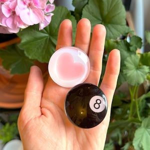 May include: Two glass paperweights, one with a pink heart design and the other with a black and white 8-ball design.