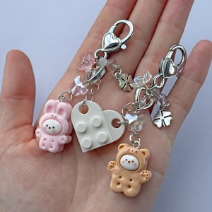 Op de afbeelding: Twee sleutelhangers met zilveren sluitingen, hartvormige bedels en kralenaccenten. Eén sleutelhanger heeft een roze konijnenfiguur, de andere een bruine berenfiguur. Een witte hartvormige bedel en doorzichtige kralen zijn ook inbegrepen.