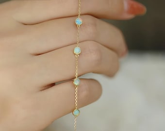 May include: A delicate gold chain bracelet with five small, round opal stones. The bracelet is on a hand, but the focus is on the jewelry.