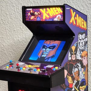 Può includere: Mini cabinato arcade X-Men con logo X-Men e grafica dei personaggi. Il cabinato ha uno schermo che mostra un personaggio, joystick, pulsanti e una base nera. Il pannello laterale presenta vari personaggi degli X-Men.