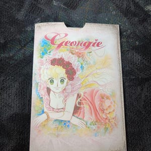 Könnte beinhalten: Ein Vintage-Buchcover mit einer Comic-Illustration einer jungen Frau mit blonden Haaren und einem rosa Kleid. Der Titel "Georgie" ist in Kursivschrift geschrieben.