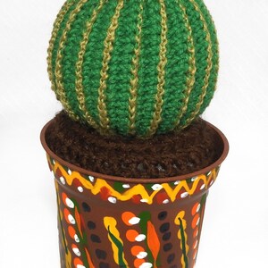 May include: A handcrafted, green crocheted cactus with gold stripes and a yellow flower, potted in a brown, hand-painted pot with colorful designs. The cactus is a unique decorative item.