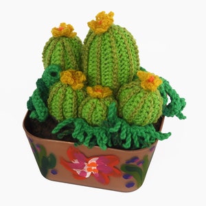 May include: A handcrafted crochet cactus arrangement in a brown painted pot. The cacti are various sizes, in shades of green, with yellow flowers. The pot is decorated with painted flowers and foliage.