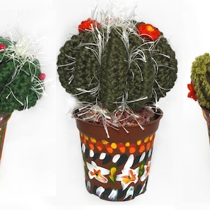 May include: Three handmade crochet cactus plants in decorative pots. The cacti are various shades of green with white accents and red flower details. The pots are brown with colorful, hand-painted designs, including geometric patterns and floral motifs.