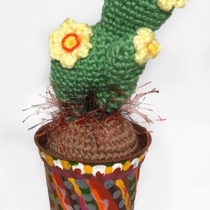May include: A handmade crochet cactus with yellow and orange flowers, set in a painted pot. The pot has a colorful, abstract design with orange, green, and gray accents. The cactus is a unique, decorative item.