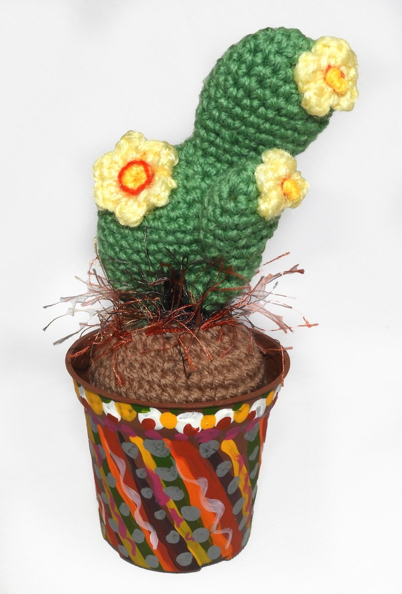 May include: A handmade crochet cactus with yellow and orange flowers, set in a painted pot. The pot has a colorful, abstract design with orange, green, and gray accents. The cactus is a unique, decorative item.