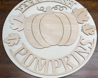 May include: A circular wooden sign featuring a central pumpkin cutout with a stem and vine. The words FARM FRESH are arched above the pumpkin, and the word PUMPKINS is arched below. Four leaf cutouts are positioned around the pumpkin design.