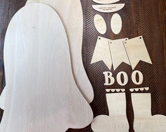 May include: A set of unfinished light-colored wood craft pieces including two large ghost-shaped cutouts, two oval shapes, three pennant flags, the letters B, O, O, two boot shapes, and two small semi-circular pieces with text printed on them.