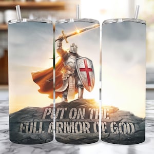 Puede incluir: Un vaso de acero inoxidable con un diseño de un caballero con armadura sosteniendo una espada y un escudo. El caballero está de pie en la cima de una colina rocosa. El texto "Ponte la armadura completa de Dios" está impreso en el vaso.