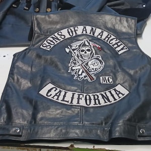 May include: Black leather vest with the "Sons of Anarchy" logo patch on the back. The patch features a skull with a scythe and the text "California". The vest has a classic biker style.