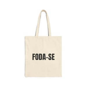 Op de afbeelding: Een beige tote bag met zwarte handvatten en de tekst "FODA-SE" in het zwart gedrukt op de voorkant.