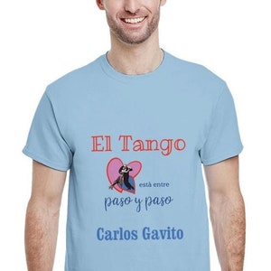 Può includere: Maglietta azzurra con un cuore rosso e una coppia che balla al suo interno. Il testo sulla maglietta recita "El Tango está entre paso y paso Carlos Gavito".