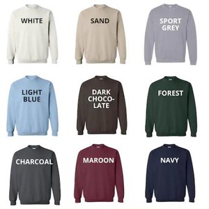 May include: A collection of crewneck sweatshirts in various colors, each labeled with its color name in white text. Colors include black, white, sand, sport grey, ash, light pink, light blue, dark chocolate, forest, military green, dark heather, charcoal, maroon, navy, and red.