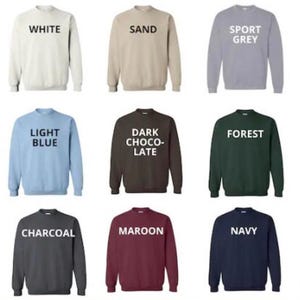 May include: A variety of crew neck sweatshirts in different colors, including black, white, sand, sport grey, ash, light pink, light blue, dark chocolate, forest, military green, dark heather, charcoal, maroon, navy, and red. Each sweatshirt has a white text label with the color name.