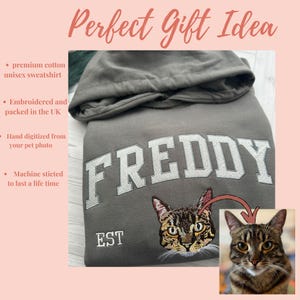 May include: A gray unisex sweatshirt with the name "FREDDY" embroidered in white block letters. Below the name is an embroidered cat face and the word "EST". A photo of the cat is in the lower right corner.