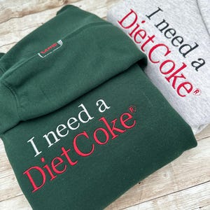 May include: Two hooded sweatshirts, one green and one gray, with the text "I need a Diet Coke&reg;" embroidered on the front. The text is in white on the gray sweatshirt and in white and red on the green sweatshirt.