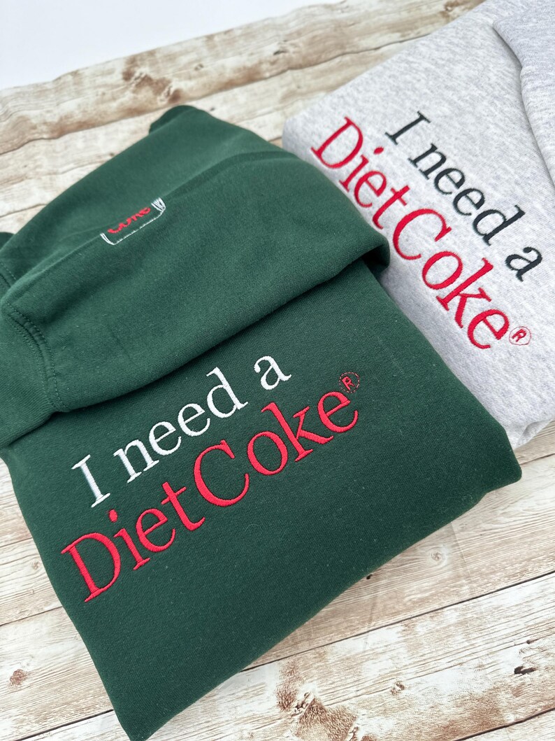May include: Two hooded sweatshirts, one green and one gray, with the text "I need a Diet Coke&reg;" embroidered on the front. The text is in white on the gray sweatshirt and in white and red on the green sweatshirt.