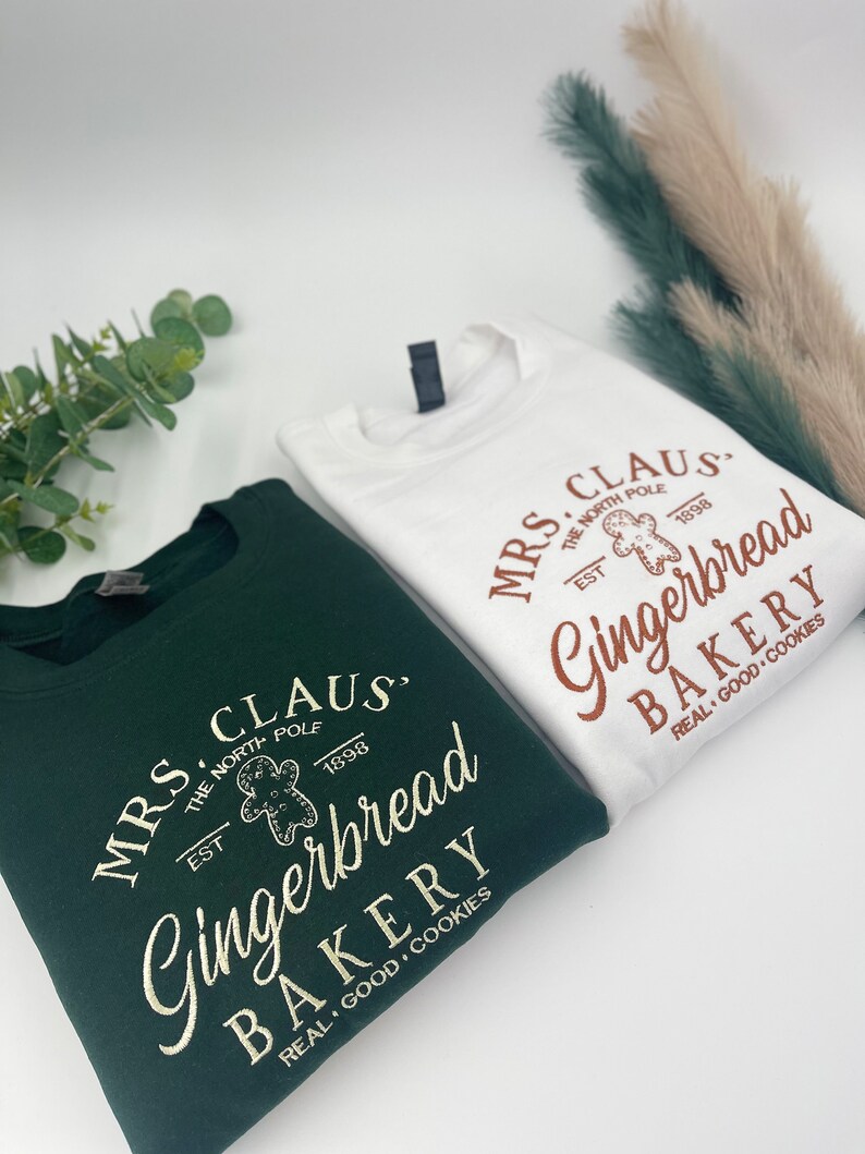 May include: Two sweatshirts, one white and one dark green, with the text "MRS. CLAUS Gingerbread BAKERY" and a gingerbread man graphic. The text includes "THE NORTH POLE EST 1898" and "REAL GOOD COOKIES".