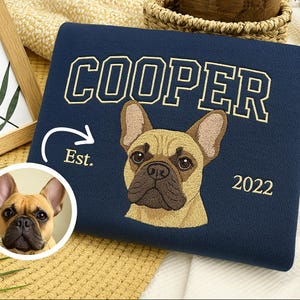 May include: Navy blue sweatshirt with the name "COOPER" embroidered in gold. Features an embroidered image of a French Bulldog and the year "2022". Includes a small circular image of the dog and the word "Est."