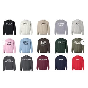 May include: A collection of crewneck sweatshirts in various colors, including black, white, sand, sport grey, ash, light pink, light blue, dark chocolate, forest, military green, dark heather, charcoal, maroon, navy, and red. Each sweatshirt has the color name printed on it.